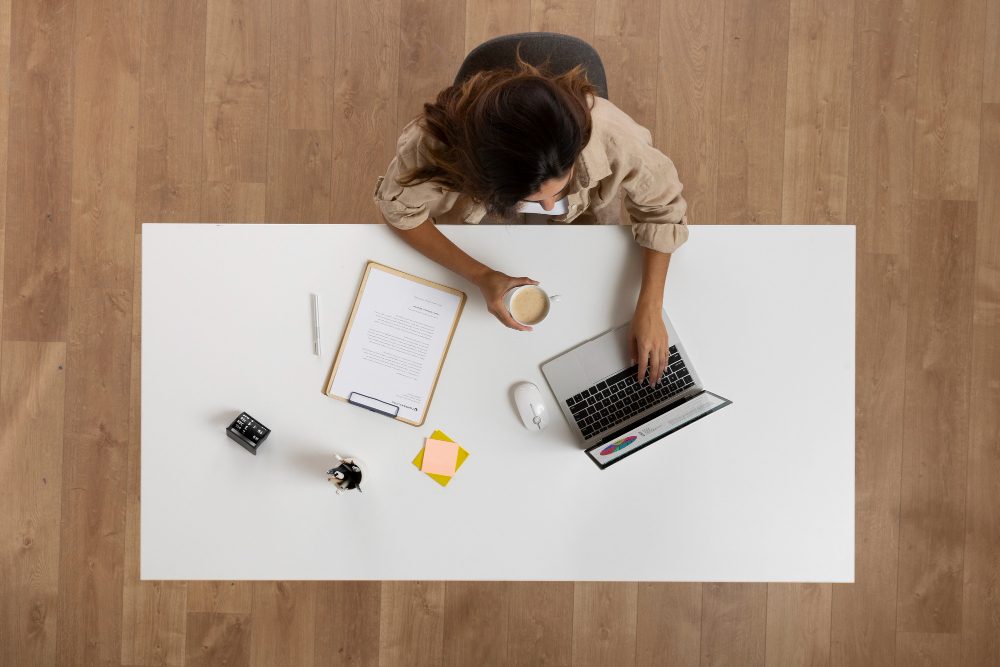 Overhead view of a workspace with a laptop, planning documents and a cup of coffee